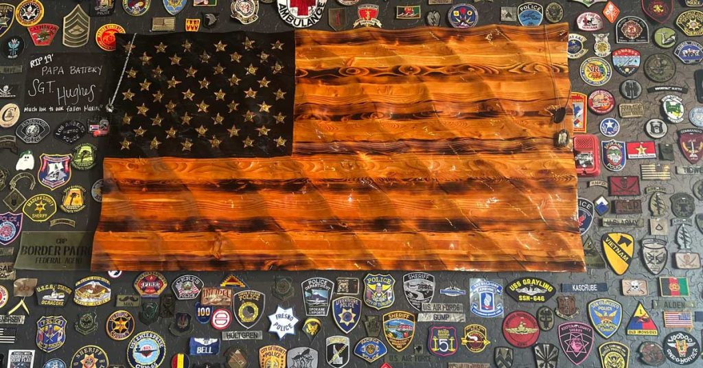 Wooden American flag displayed on a table with military and first responder service patches, symbolizing unity and honor at The Veterans Club meeting location.